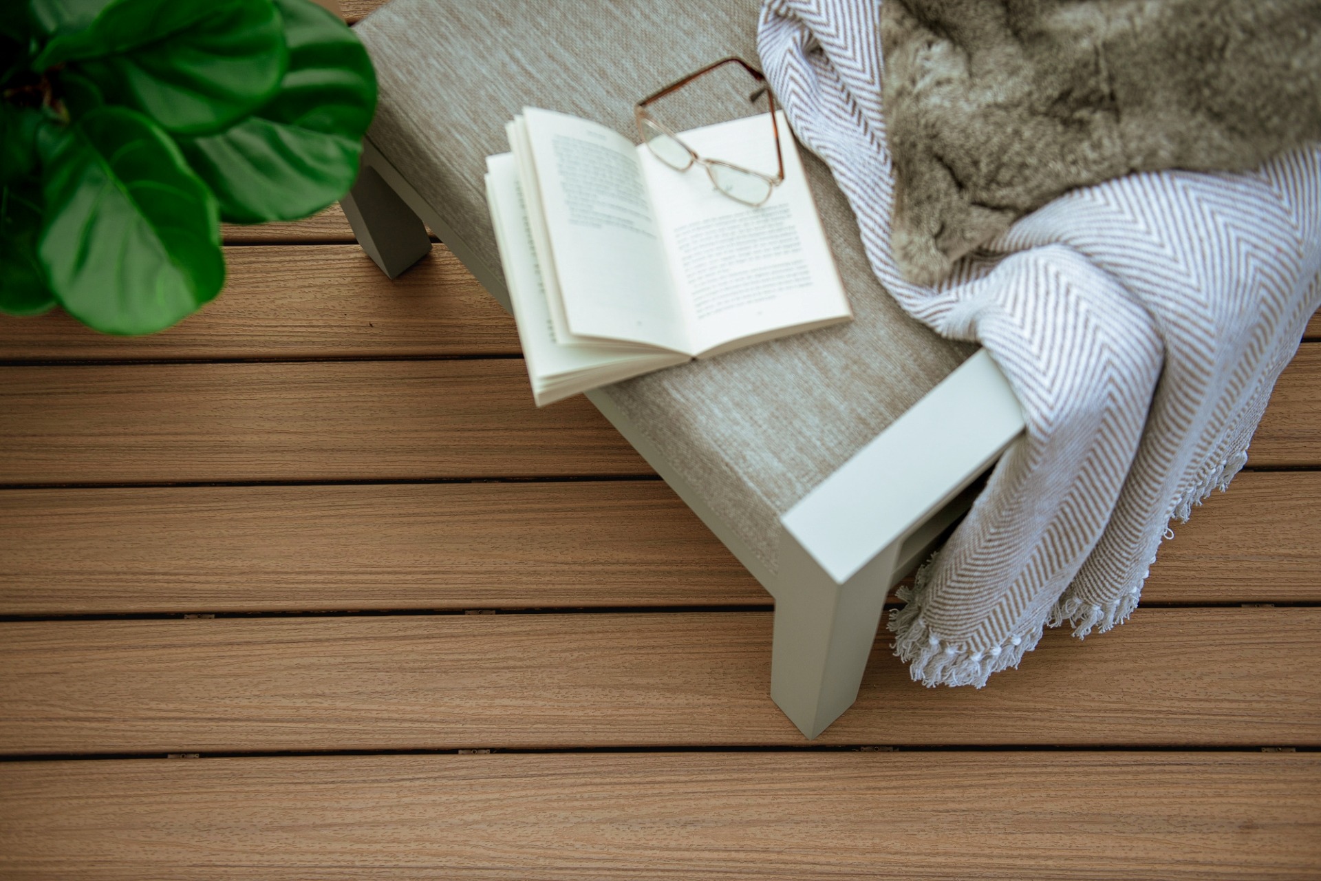 Close-up top view of Trex Enhance Golden Hour composite decking with a bench, open book, glasses, and blanket, highlighting the smooth golden-brown board texture.