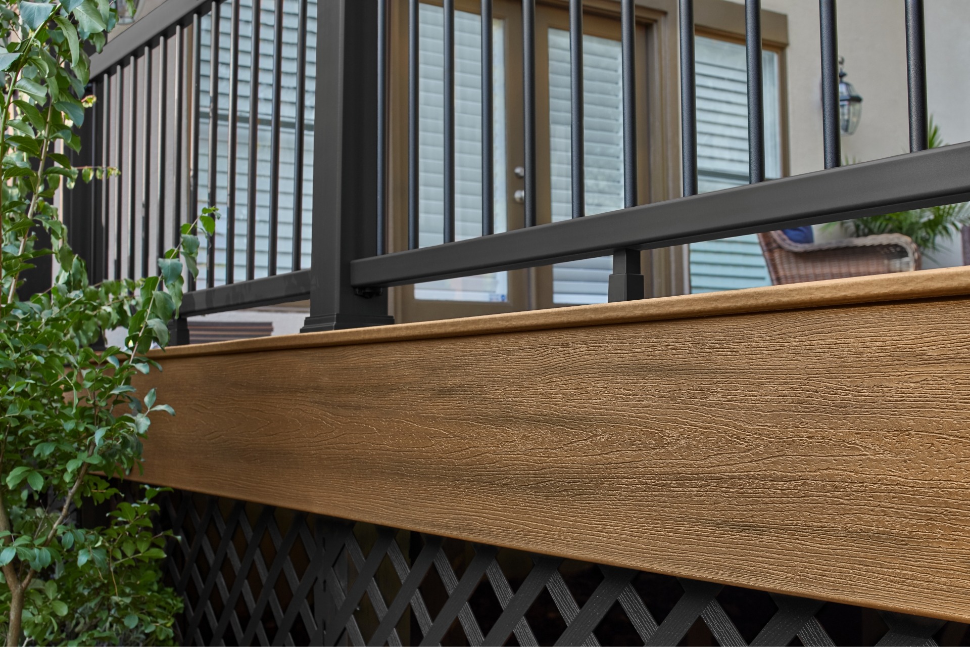 Close-up side view of Trex Enhance Golden Hour fascia board beneath a black aluminum railing, showcasing realistic wood-grain texture and warm golden-brown finish.