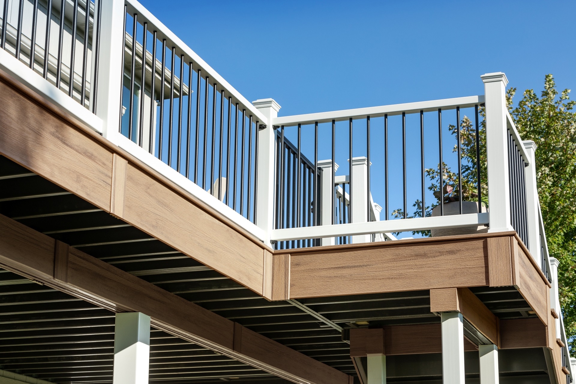 Elevated deck finished with Trex Enhance Golden Hour composite fascia and white posts with black aluminum balusters, shown under bright sunlight and clear blue sky.