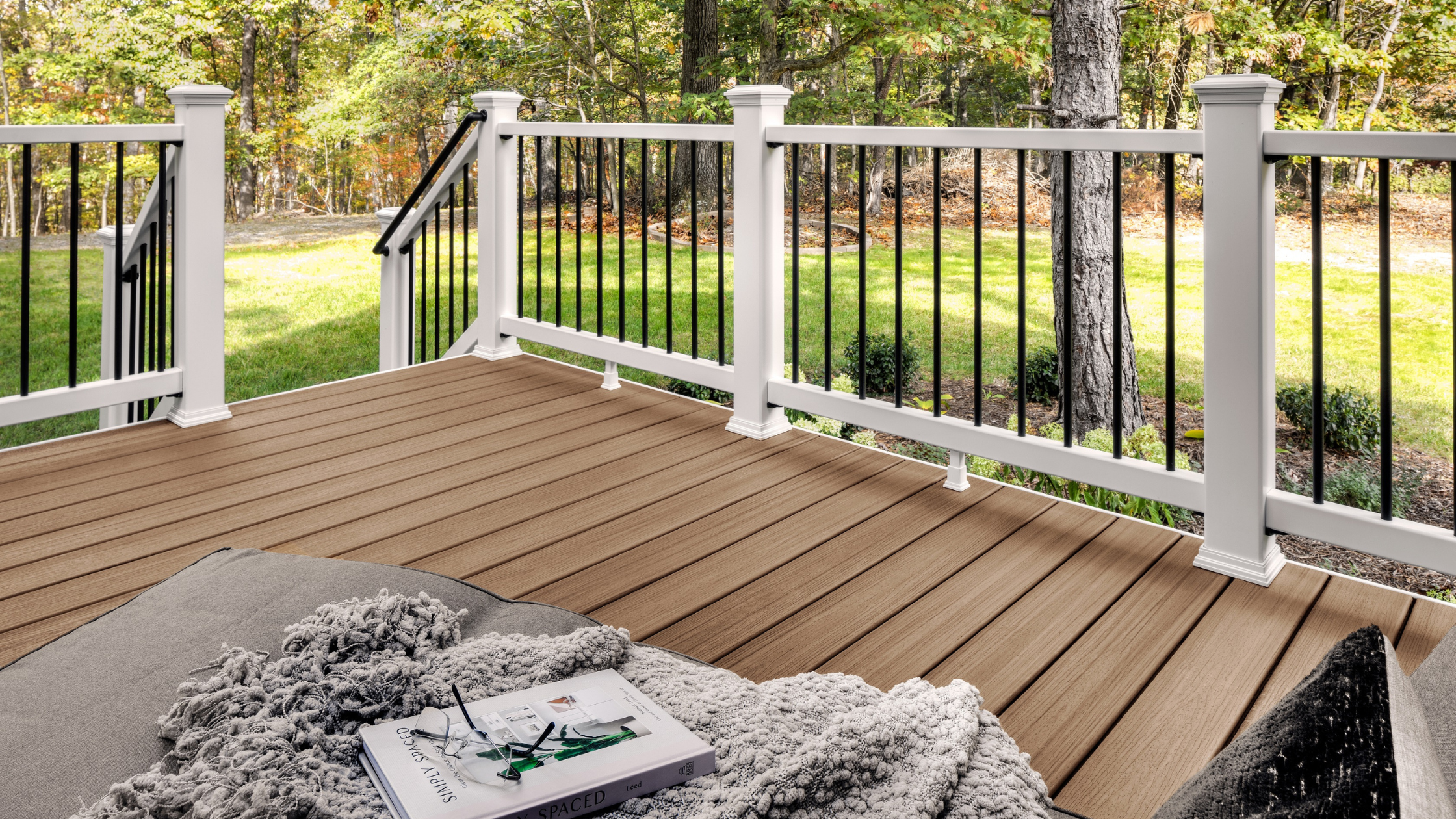 A cozy backyard deck built with Trex Enhance Golden Hour, showing warm golden-brown boards with a natural wood-grain texture. The space features white posts, black railings, and soft neutral décor, highlighting the rich tone and realistic finish of the Trex Enhance colors collection.