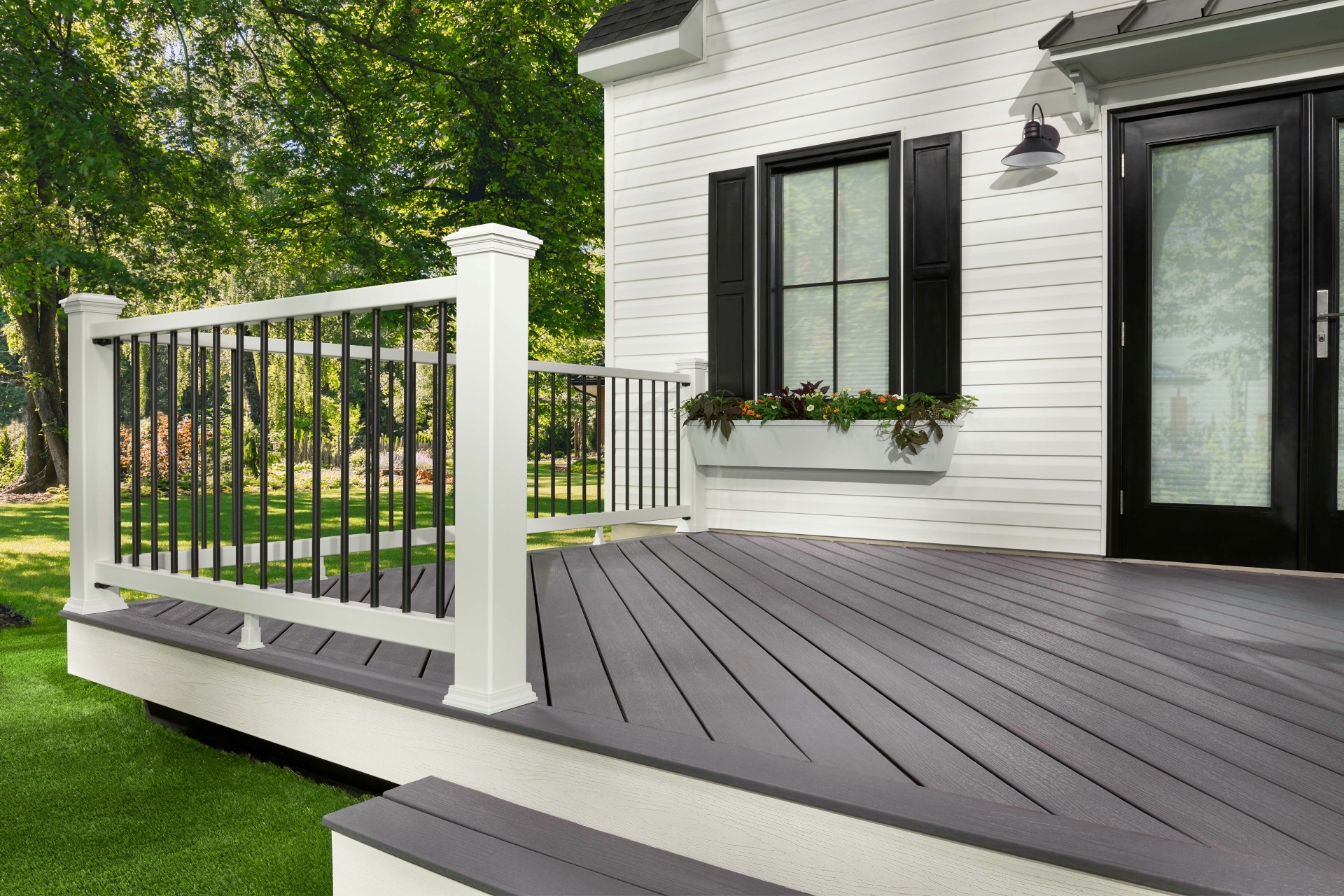 Front porch deck built with Trex Enhance Pebble Beach composite decking in a light gray tone, featuring white posts, black balusters, and a matching white home exterior with black trim.