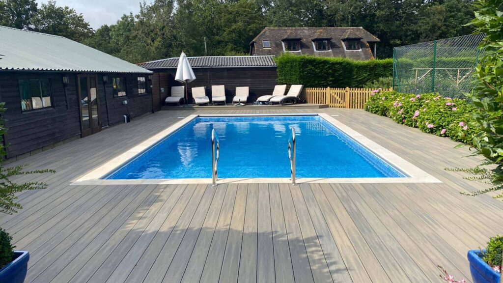 Light gray composite deck around rectangular backyard pool with lounge chairs.