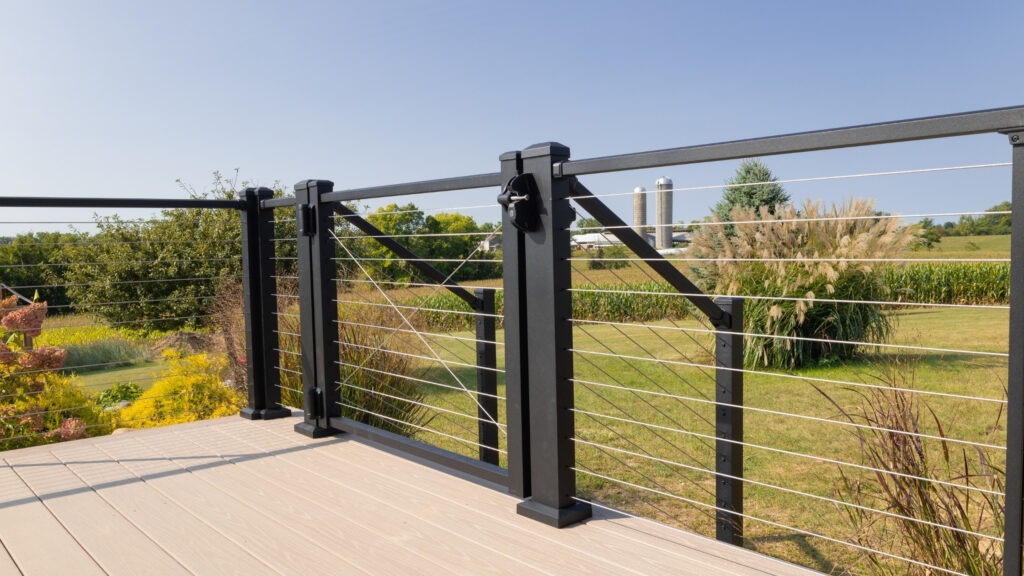 Black cable deck railing with gate overlooking scenic farmland, elegant and secure example of cable deck railing ideas for open decks.