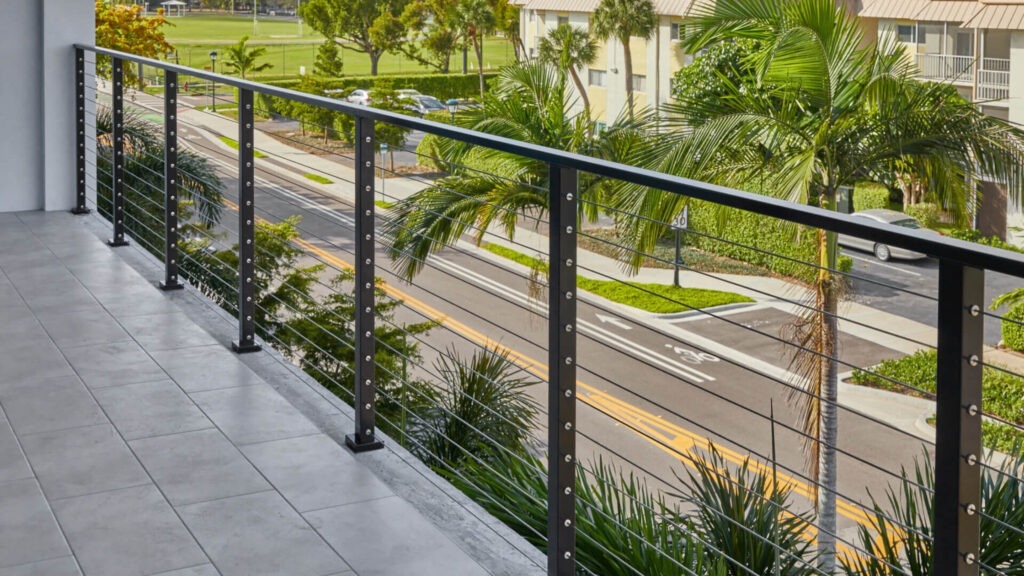 Black aluminum balcony railing with stainless cables overlooking palm trees, stylish deck cable railing ideas for tropical settings.