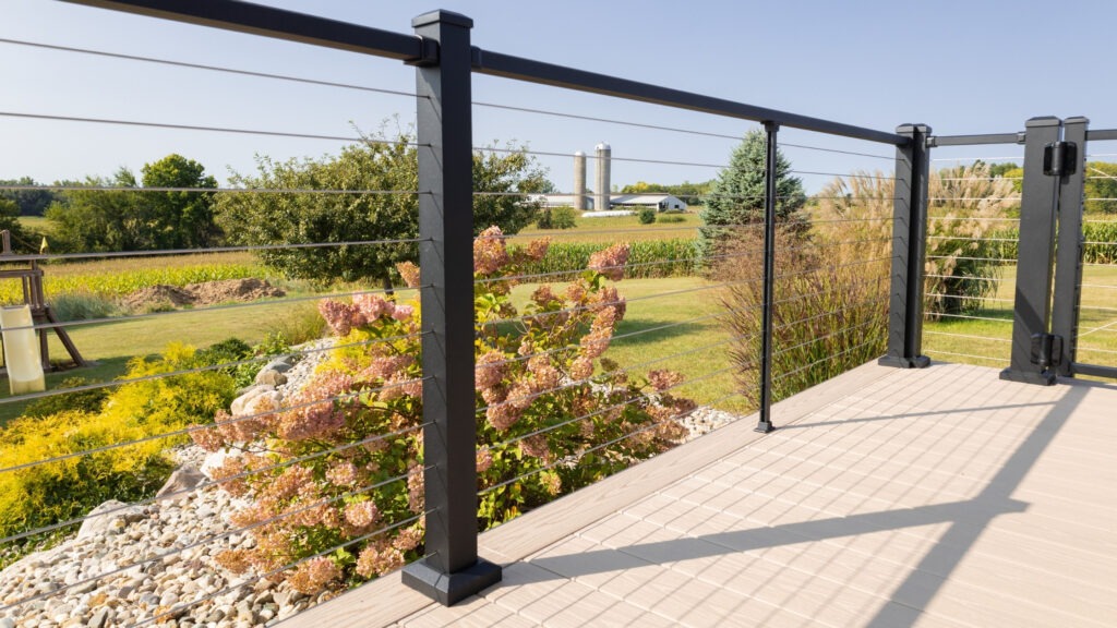 Black aluminum cable railing with composite deck and open rural background, stylish deck cable railing ideas for countryside views.