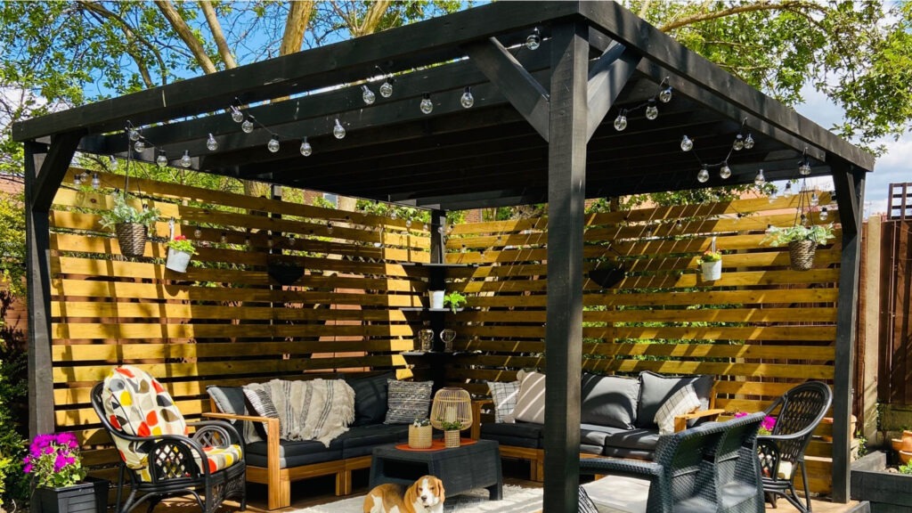 Black pergola with privacy screen and string lights on modern patio.
