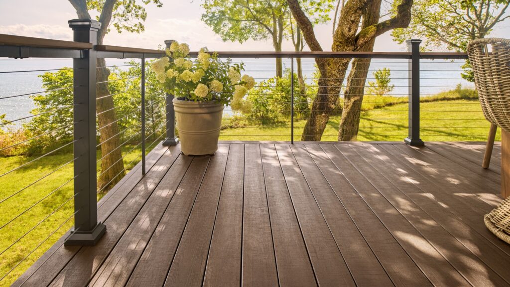 Brown composite deck with black aluminum cable railing overlooking lake and green landscape.