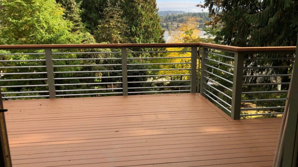 Brown composite deck with gray aluminum horizontal railing and wood top rail surrounded by green trees.