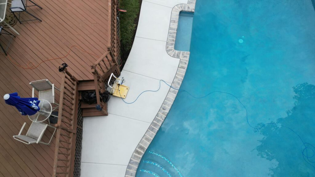 Aerial view of inground pool with brown wood deck and concrete pool edge.