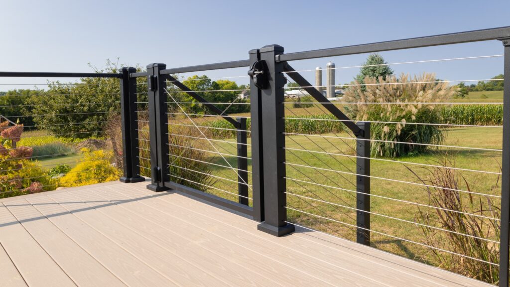 Composite deck with stainless steel cable railing and black aluminum gate overlooking open backyard.