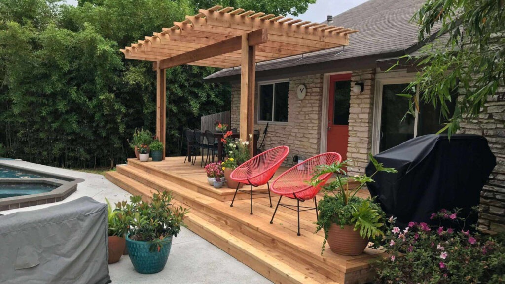 Cedar pergola over wood deck with red patio chairs, potted plants, and poolside seating area.