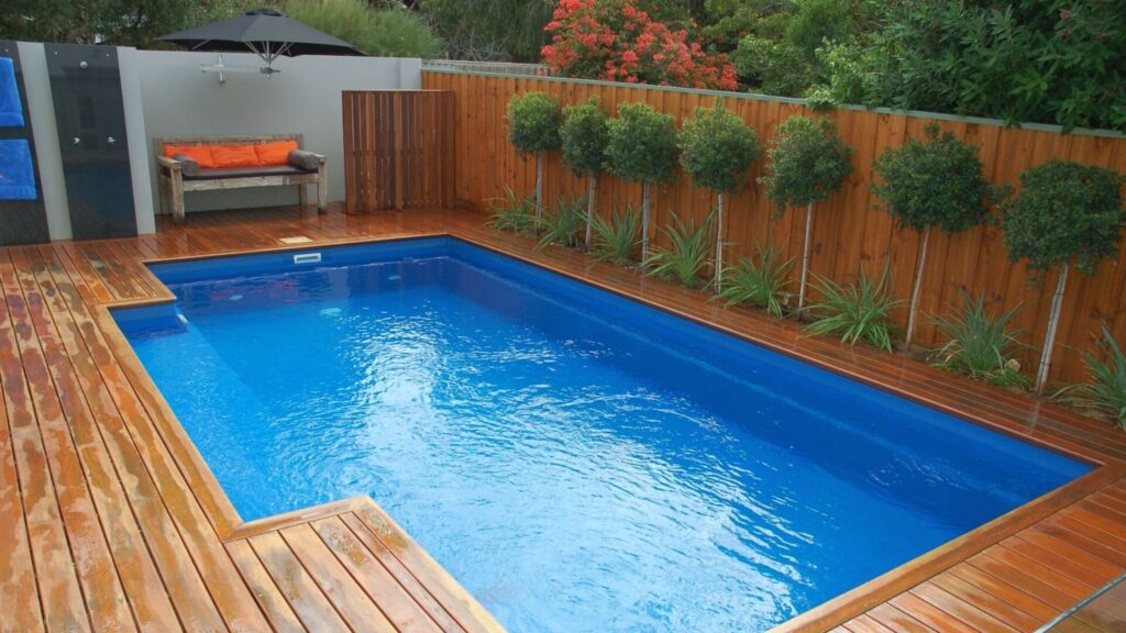 Cedar wood pool deck with privacy fence and small trees along the border.