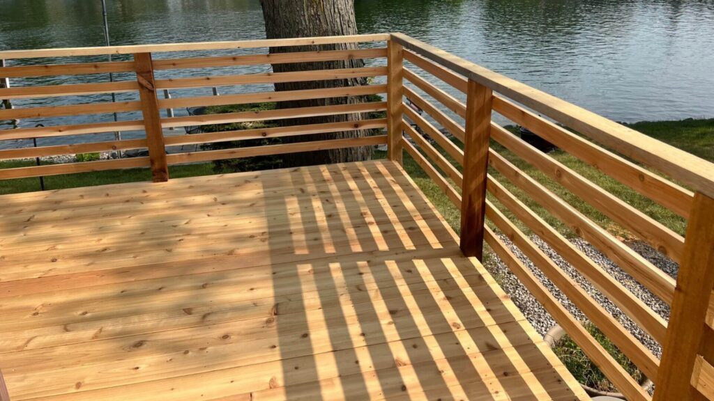 Cedar horizontal wood deck railing overlooking lake with natural water reflection.