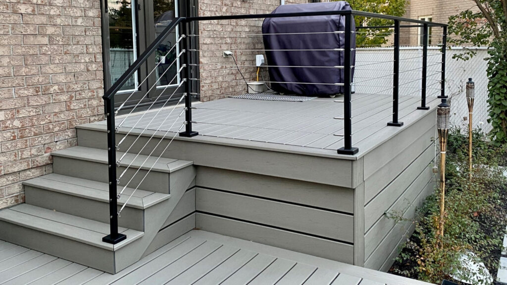 Small composite deck with black cable railing and gray boards, functional cable railing ideas for deck design in tight spaces.