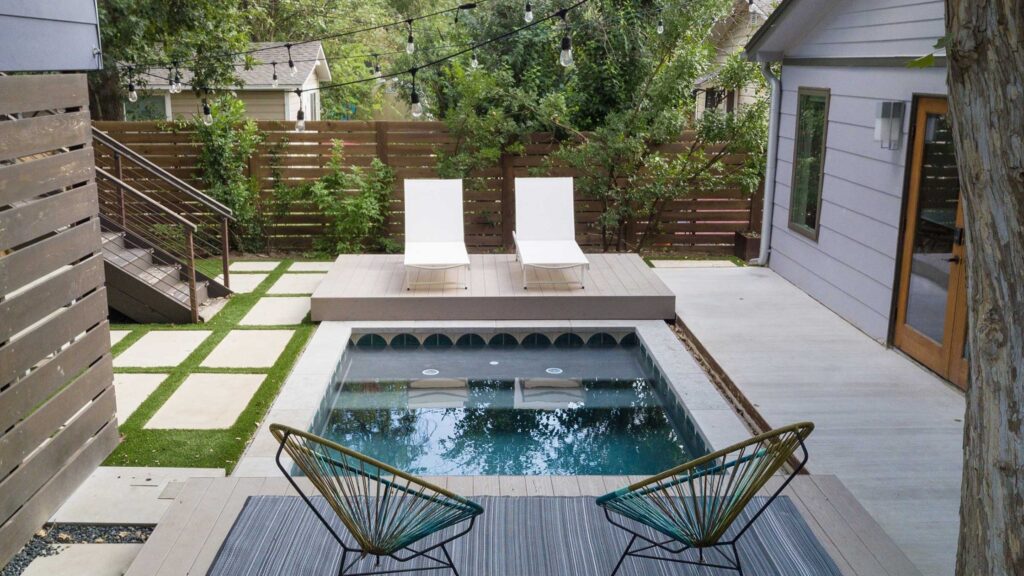 Small inground pool with modern deck, privacy fence, and lounge chairs.