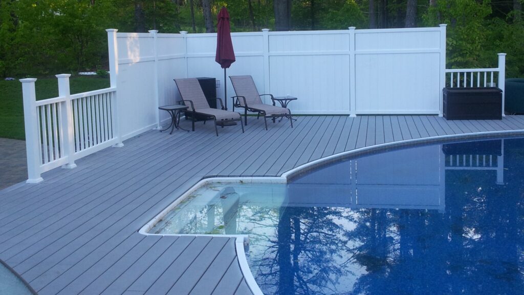 Curved gray composite pool deck with white privacy fence and outdoor seating area.
