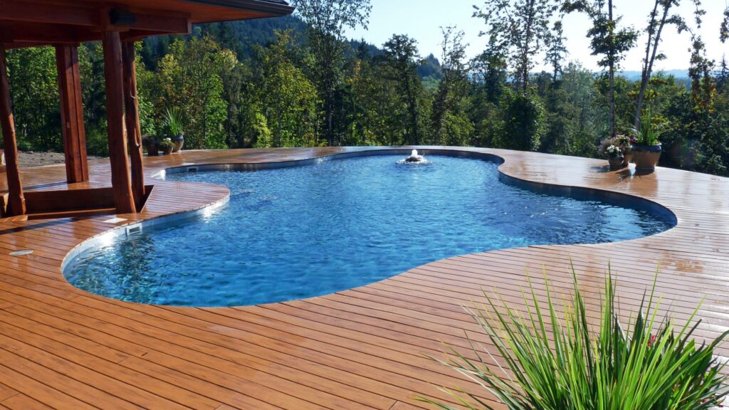 Curved wooden deck surrounding a freeform inground pool with trees in the background.