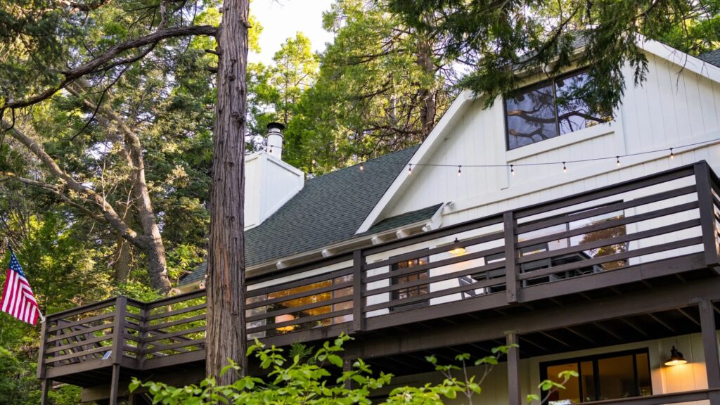 Dark brown horizontal wood deck railing on forest cabin with string lights and trees.