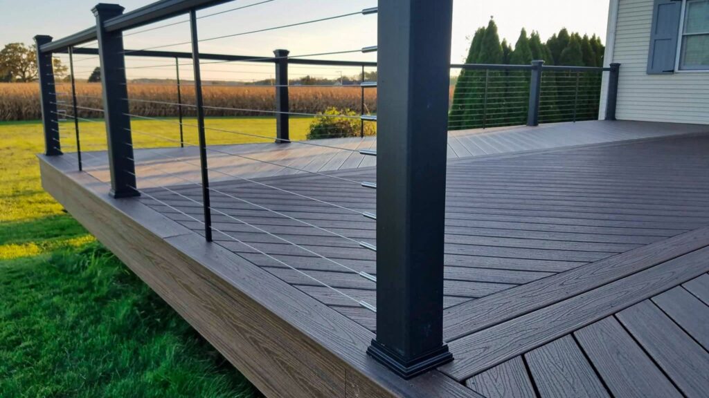Dark brown composite deck with black aluminum cable railing overlooking green backyard.
