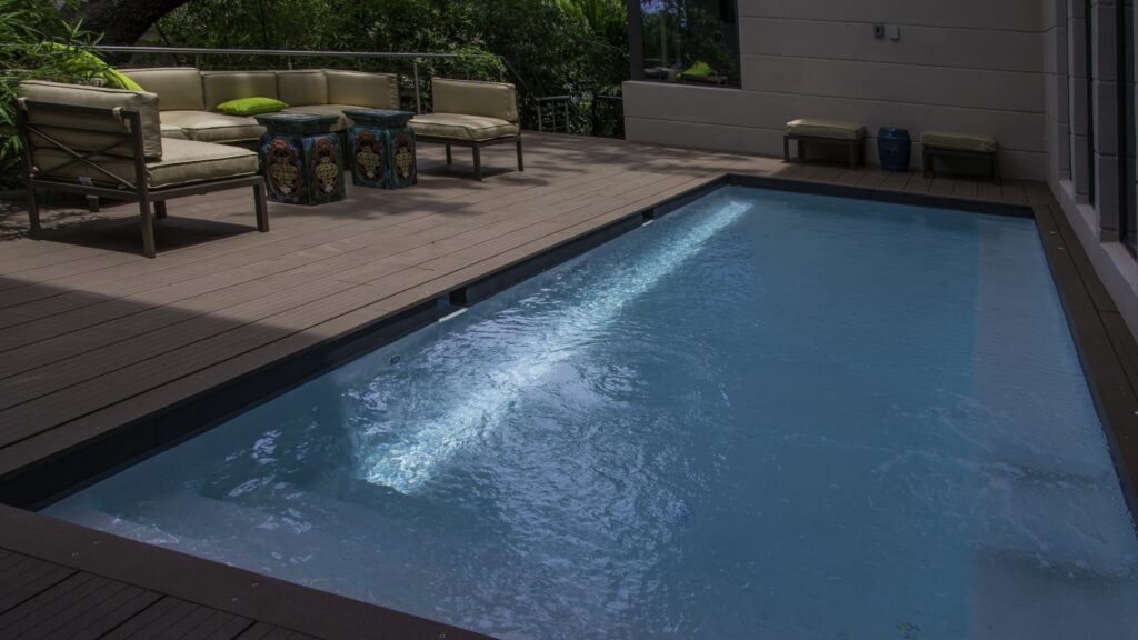 Dark composite deck with small inground pool and beige outdoor furniture.