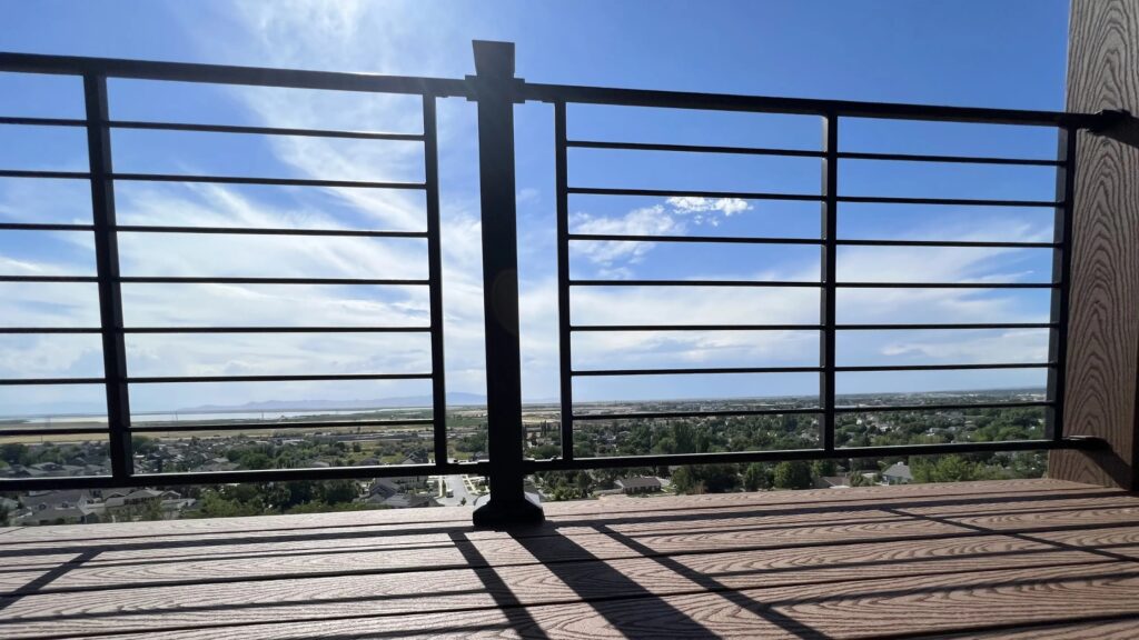 Elevated deck with black horizontal metal railing overlooking panoramic city and sky view.