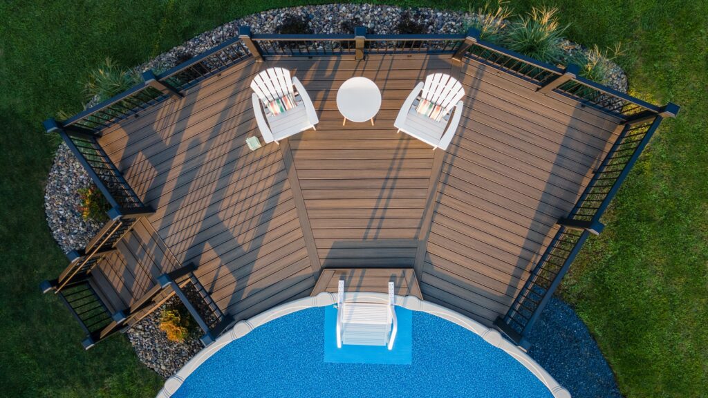 Elevated pool deck with dark brown composite boards, black railings, and backyard setting.