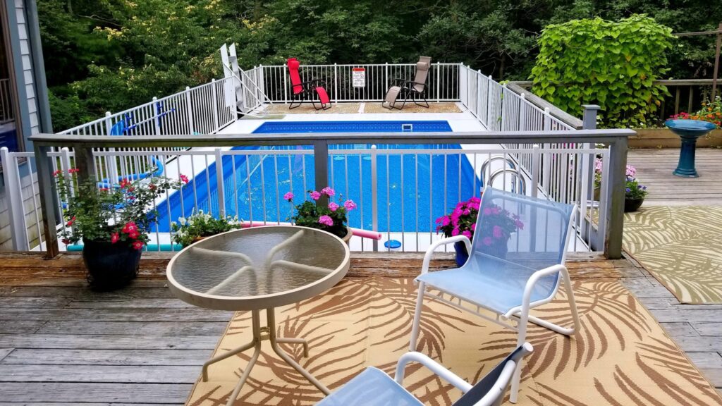 Elevated above ground pool deck with white railings, flowers, and patio furniture.