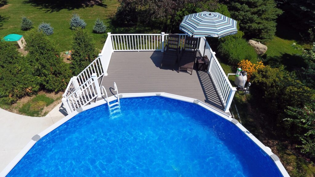 Elevated round above ground pool with white railings, seating area, and umbrella shade.