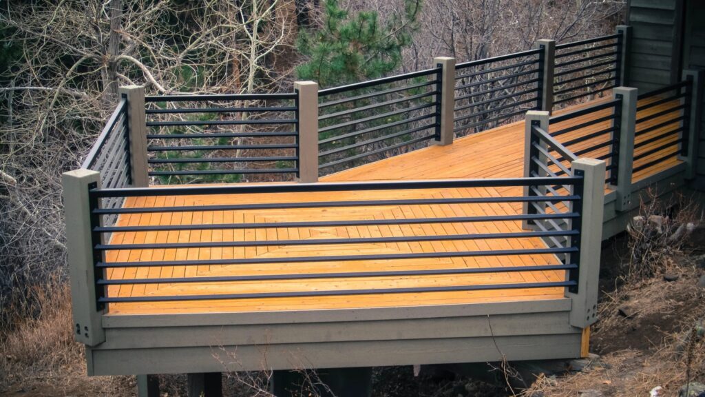 Elevated wooden deck with horizontal black aluminum railing surrounded by forest landscape.