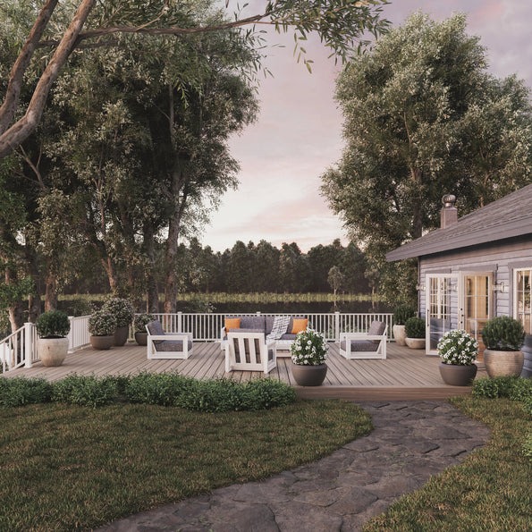 A wide angled view of a spacious backyard deck finished in Fiberon ArmorGuard Aspen Gray. The deck is surrounded by potted plants, white railings, and outdoor seating arranged to face a wooded landscape. The cool gray boards give the space an airy, natural aesthetic.