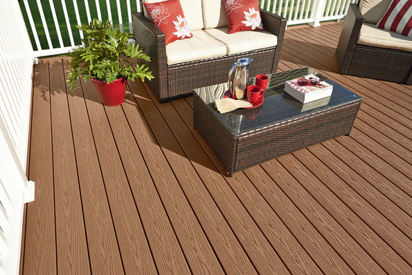 An outdoor deck built with Fiberon Good Life Cabin boards, showcasing their rich medium-brown tone and traditional stained appearance. The space features wicker seating with cream cushions and red accents, highlighting the deck’s warm, inviting feel.