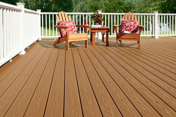 A backyard deck constructed with Fiberon Good Life Cabin decking, displaying its smooth, wood-toned surface and solid color throughout. Wooden Adirondack chairs and red patterned cushions sit on the deck, emphasizing its classic, timeless style.