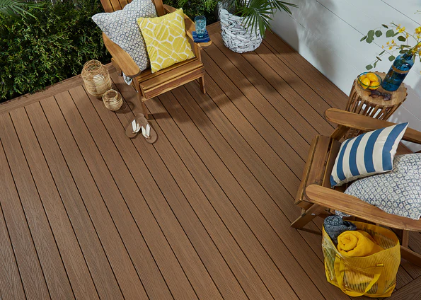 Outdoor deck built with Fiberon Good Life Tuscan Villa boards, showing warm brown multi-tonal planks beneath wooden chairs and yellow-accented décor; the surface features realistic grain embossing and a matte finish.