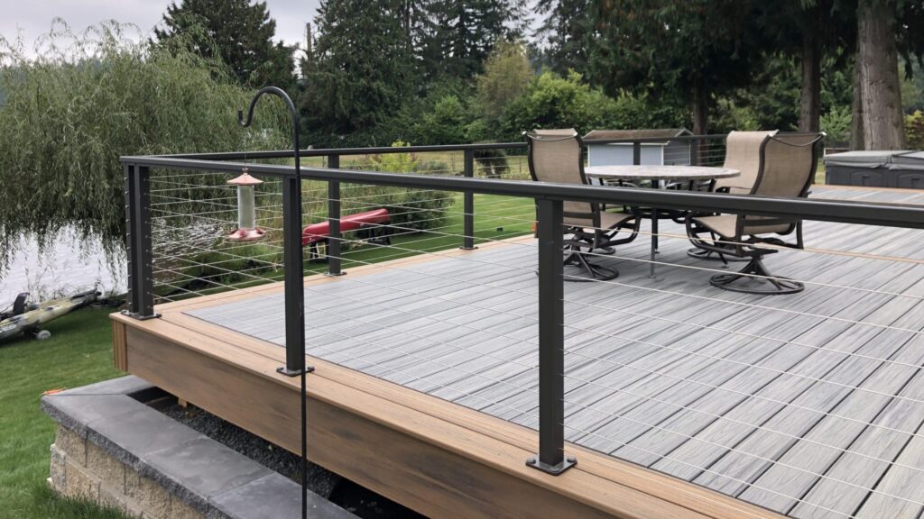 Gray composite deck with black cable railing and outdoor dining furniture, stylish modern cable deck railing ideas.