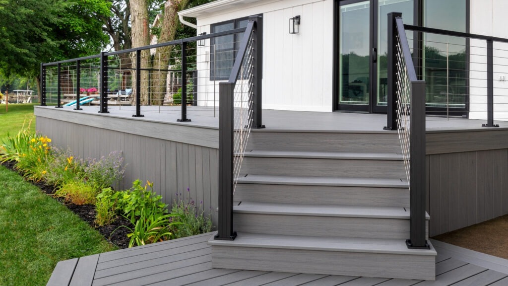 Gray composite deck with black aluminum cable railing and white house, modern deck cable railing ideas for clean outdoor design.