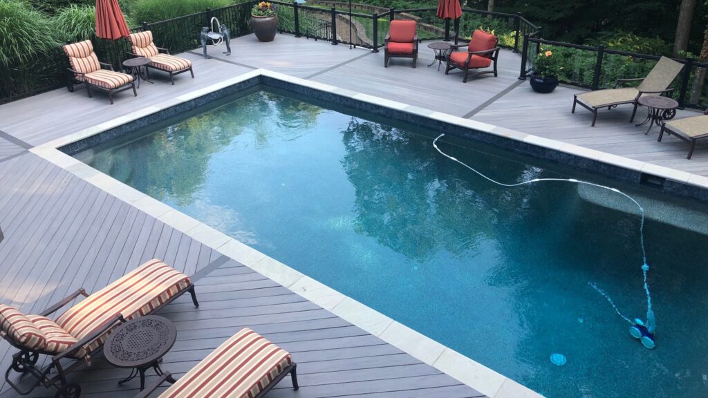 Gray composite deck with black railings and inground pool featuring red lounge chairs.