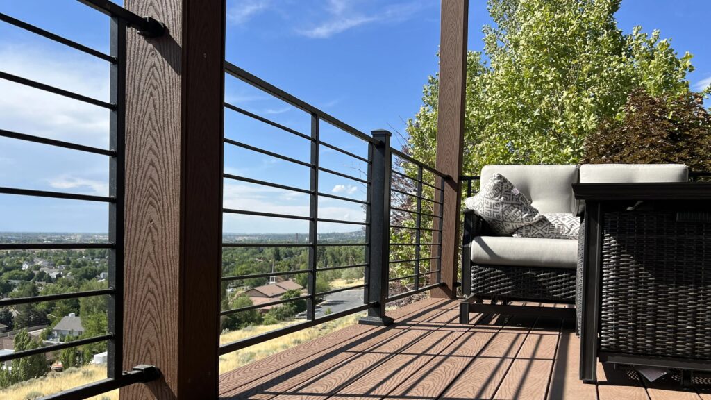 Modern hillside deck with horizontal metal railing and brown composite boards overlooking scenic residential view.