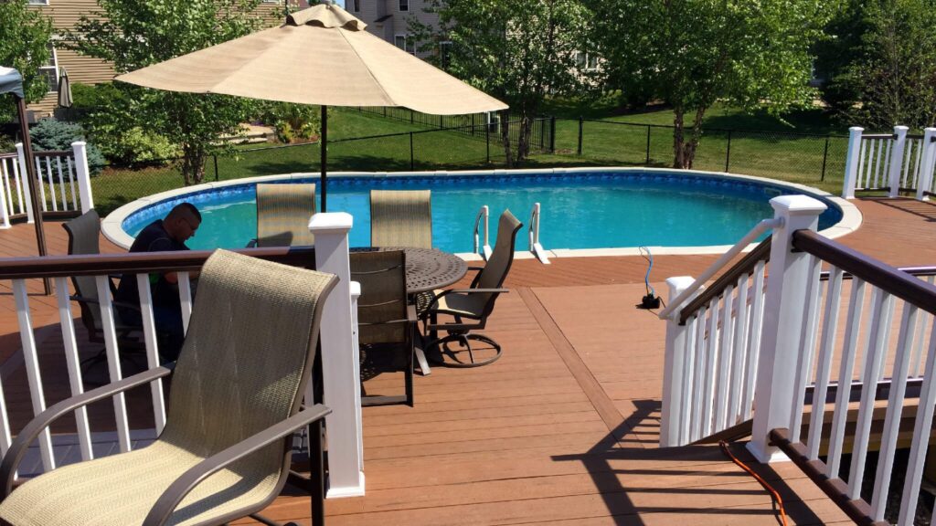 Large round above ground pool with surrounding wood deck, white railings, and umbrella seating.