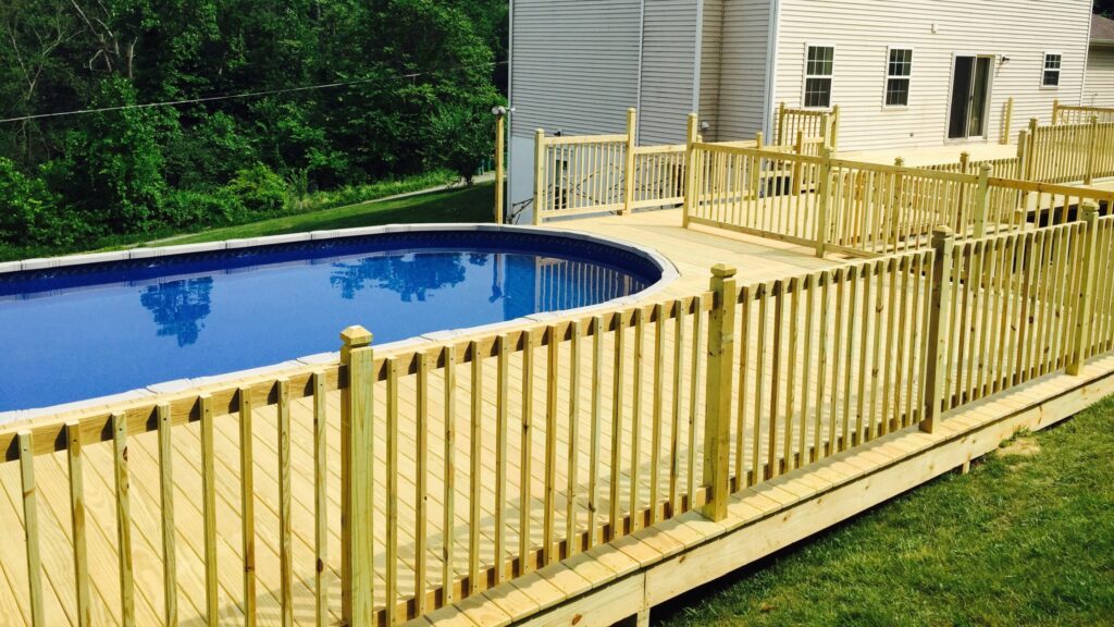 Large yellow wood deck with fenced railing surrounding blue backyard pool.