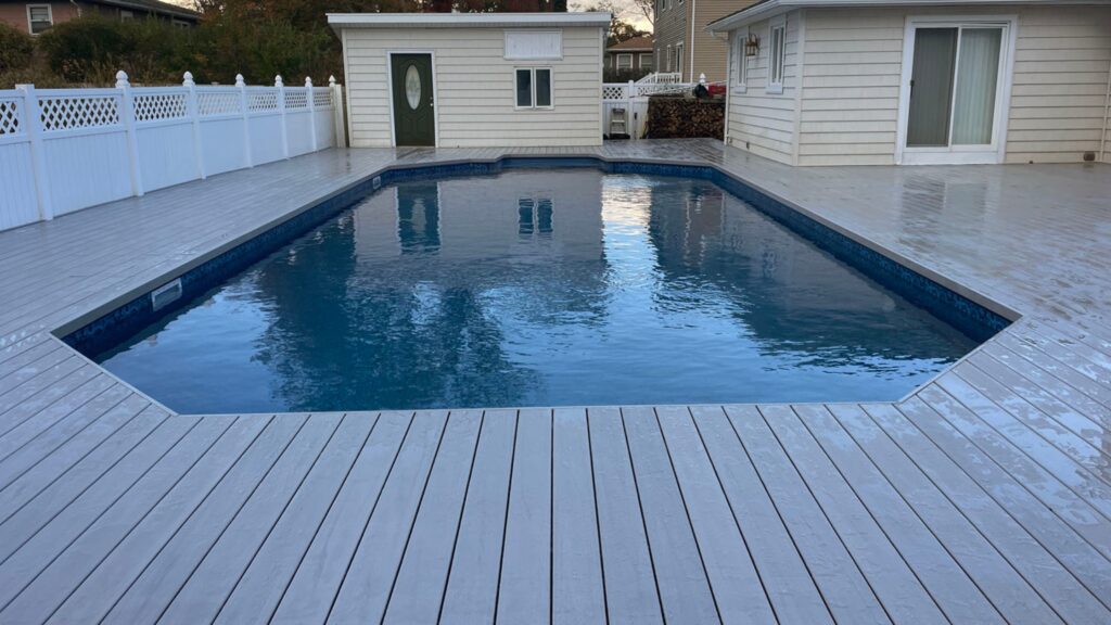 Light gray composite deck surrounding a rectangular inground pool with white fencing.