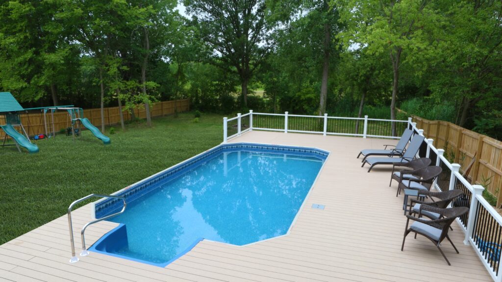 Light tan composite pool deck with white railings, lounge chairs, and backyard landscape.