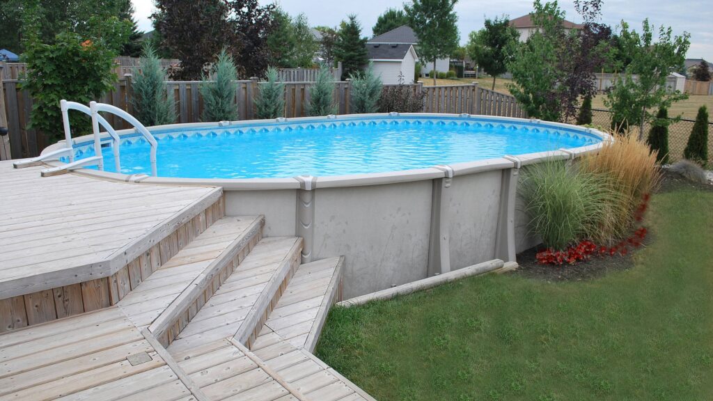 Light wood above-ground pool deck with stairs, blue pool, and green backyard view.