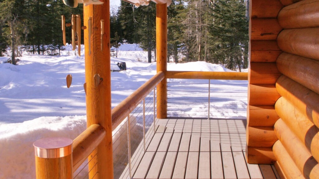 Winter cabin deck with stainless steel cable railing and log posts, rustic mountain example of cable deck railing ideas.
