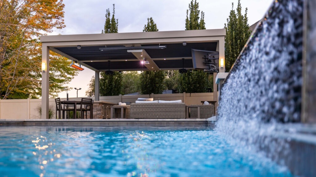Luxury pergola beside pool with waterfall feature, lounge furniture, and outdoor lighting.