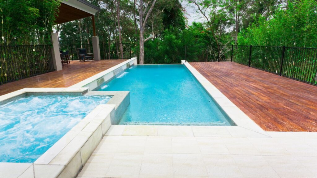 Luxury wooden pool deck with hot tub and natural landscaping.