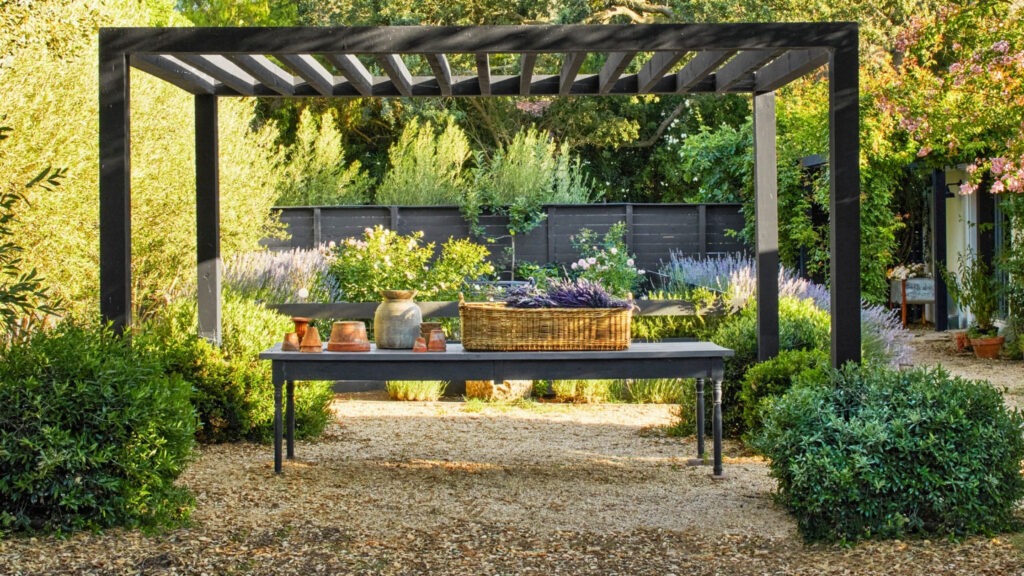 Black minimalist pergola in garden with potting table, lavender plants, and decorative vases.
