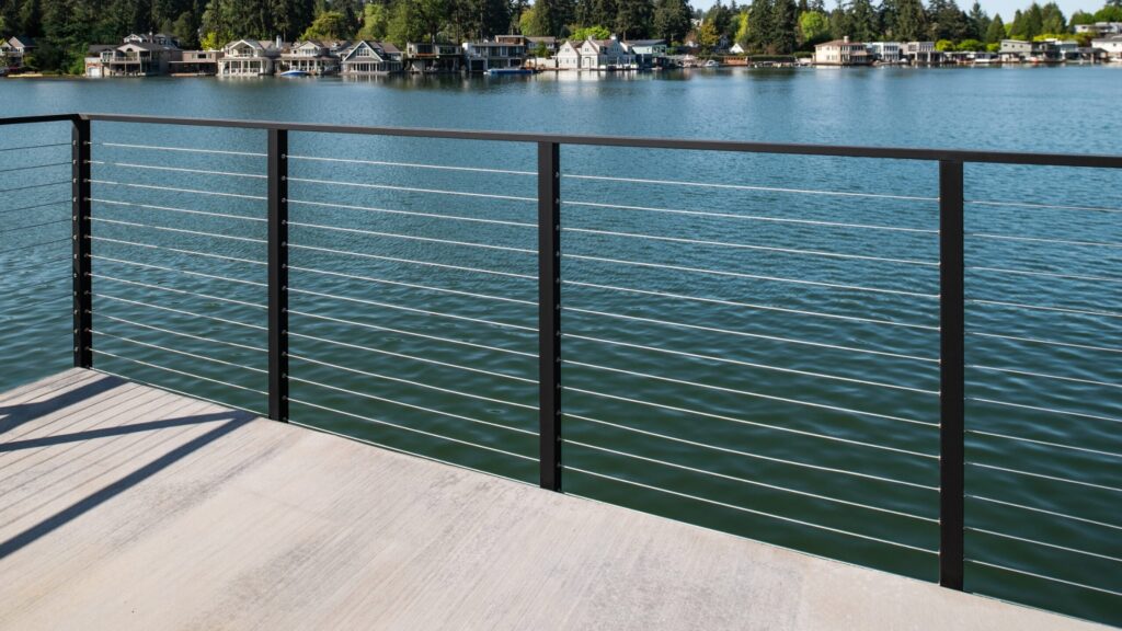 Waterfront modern horizontal cable deck railing with black aluminum posts and stainless-steel cables.