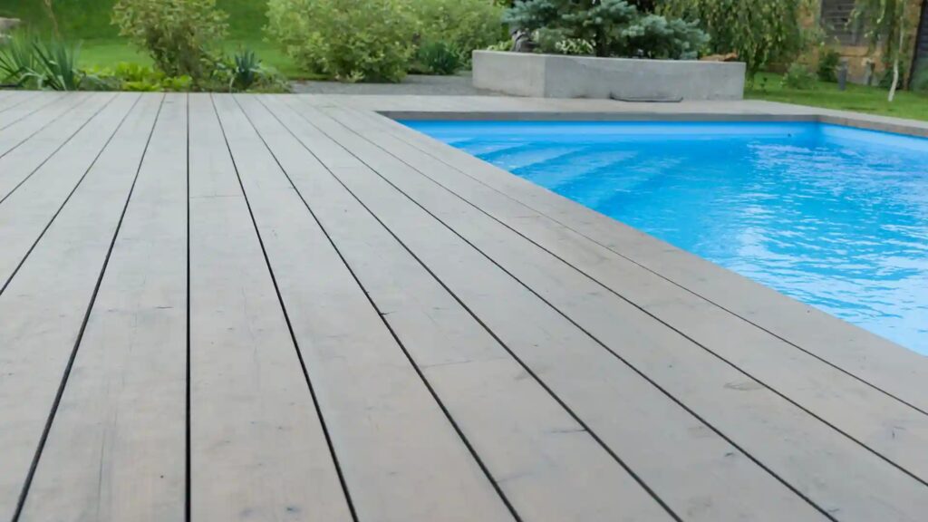 Light gray composite deck surrounding a rectangular inground pool with green landscaping.