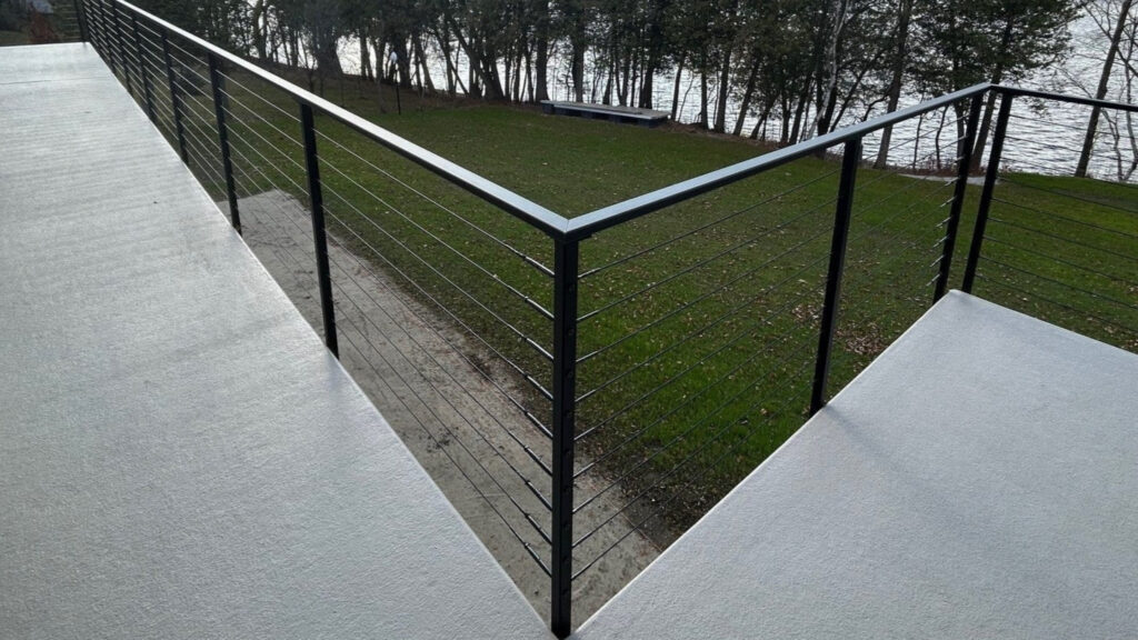 Minimalist balcony with black cable railing overlooking water, modern example of cable deck railing ideas.