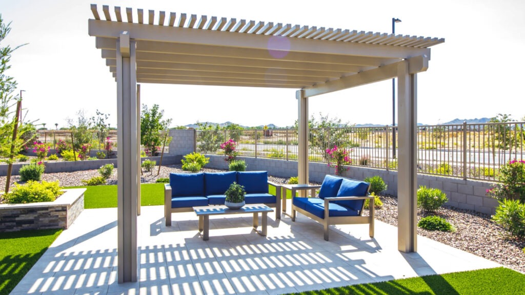 Modern aluminum pergola with blue outdoor seating on tiled patio in sunny backyard.